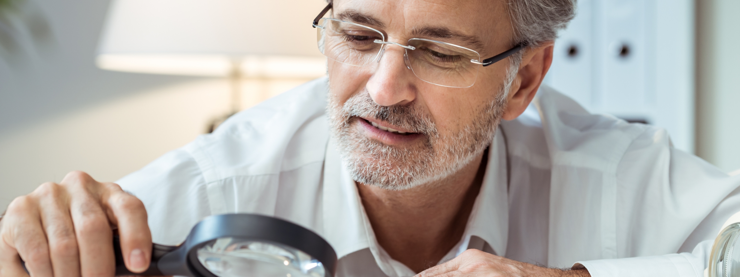Mann mit Lupe liest ein Dokument auf dem Tisch